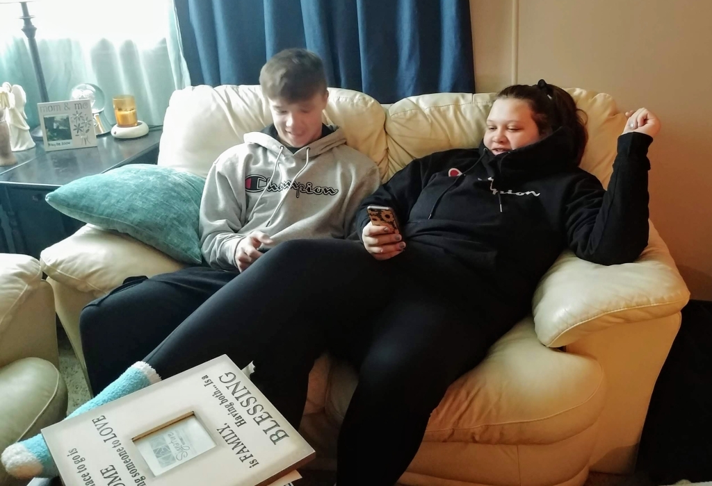 brother and sister on couch playing on their phones